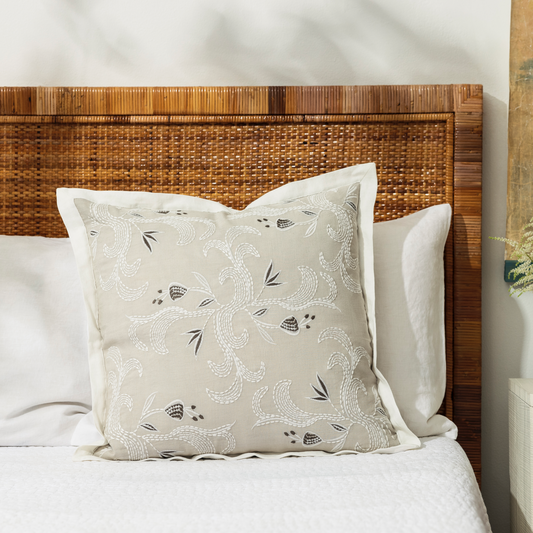 marseille dove pillow against a white bedding background with a cane headboard