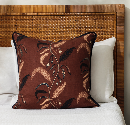 tuileries terracotta pillow on a bed with white sheets